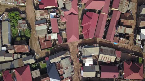 Aerial-top-down-to-cyclist-on-street-and-metal-roof-homes-in-Bukasa,-Kampala-city,-Uganda