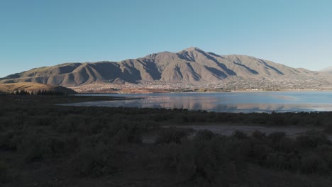 Aerial-Pan-Overlooking-Water-In-Desert-Landscape-With-Mountains-Beyond-The-Water-In-The-Distance