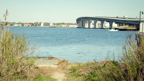 Caminando-Hacia-El-Puente-Hacia-Ocean-City,-Con-Edificios,-Agua-Y-Arbustos.