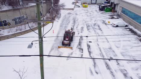 Tractor-with-snow-plow-cleaning-private-parking-lot-in-Canada,-aerial-view