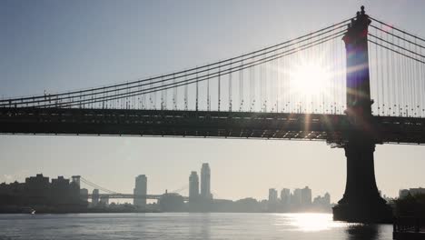 Puente-De-Manhattan-De-La-Ciudad-De-Nueva-York-Desde-Abajo-Con-El-East-River-Y-La-Ciudad-Al-Fondo-Con-El-Amanecer-Brillando-A-Través-Del-Puente