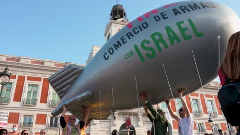 In-Madrid,-Spain,-at-Puerta-del-Sol-,-protesters-advocating-for-Palestine,-some-with-a-balloon-depicting-a-bomb,-call-for-an-end-to-arms-sales-to-Israel