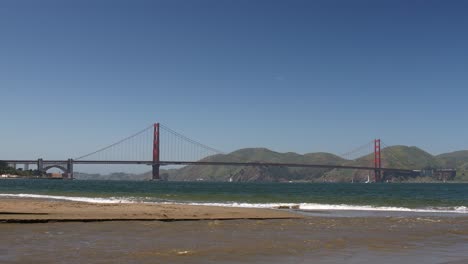 Golden-Gate-Bridge-Mit-Wasser,-Das-Den-Strand-Hinunter-In-Die-Bucht-Läuft,-Mit-Blauem-Himmel,-Untersicht,-San-Francisco,-Kalifornien,-USA