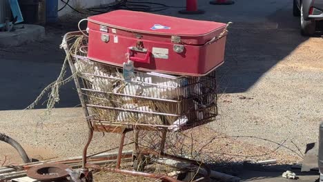 Wide-shot-homeless-person's-old-red-suitcase-on-trolley-full-of-rubbish