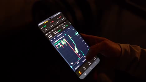 A-person-analyzes-cryptocurrency-charts-on-a-smartphone-in-low-light
