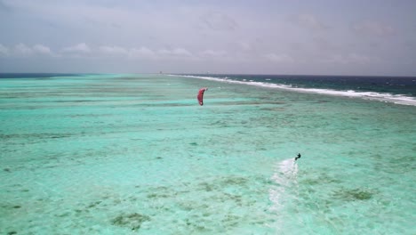 A-lone-kite-surfer-gliding-over-the-vibrant,-turquoise-waters-of-los-roques-with-a-distant-barrier-reef,-aerial-view
