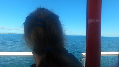 A-woman,-facing-away,-enjoys-the-serene-beauty-of-the-calm-ocean-while-traveling-on-busselton-jetty-train-under-a-bright-blue-sky