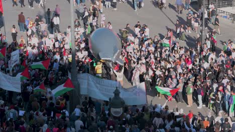 Pro-Palestine-protesters,-holding-a-balloon-depicting-a-bomb-and-Palestine-flags,-take-part-in-a-demonstration-to-demand-an-end-to-arms-sales-to-Israel-at-Puerta-del-Sol-in-Madrid,-Spain