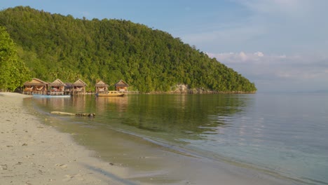 Ruhiger-Strand-Auf-Der-Insel-Kri-Im-Raja-Ampat-Archipel,-Indonesien,-Mit-Holzhütten-Entlang-Der-Küste-Vor-Einer-üppig-Grünen-Kulisse