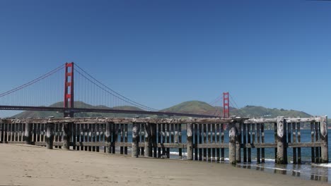 Golden-Gate-Beach-with-Wooden-Pier-and-the-Famous-Golden-Gate-Bridge-Against-Cloudless-Blue-Skies,-San-Francisco,-California,-USA