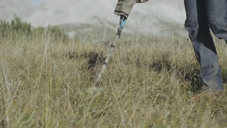 Tracking-Shot-Of-Subject-Walking-Through-Mountain-Meadow-Grasses-With-Metal-Detector