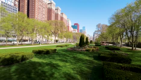 Imágenes-Aéreas-De-Drones-FPV-De-Un-Sereno-Parque-Urbano-Con-Césped-Bien-Cuidado,-Flores-Y-Edificios-De-La-Ciudad-De-Chicago-Bajo-Un-Cielo-Azul-Claro