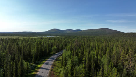 Aerial-ascending-shot-of-a-forest-road-in-front-of-the-Ounstunturit-fells,-summer-in-Lapland