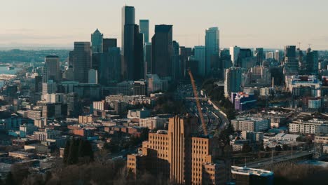 Kreisende-Drohnenaufnahme-Des-Pacific-Tower-Mit-Skyline-Von-Seattle-Und-Autobahnverkehr-Bei-Sonnenuntergang