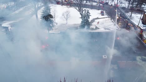 Cloud-of-smoke-above-burning-building,-extinguishing-fire-with-water-cannon-with-ladder,-aerial