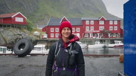 SLOW-MOTION-A-young-female-photographer-tourist-walks-towards-the-camera-with-in-background-the-red-rorbu-houses-of-the-beautiful-fisher-village-of-Å-in-the-Lofoten-Islands,-Norway