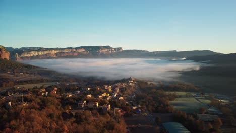 Pueblo-De-Vilanova-De-Sau-En-España-Con-Niebla-Matutina-Y-Montañas-Al-Fondo,-Vista-Aérea