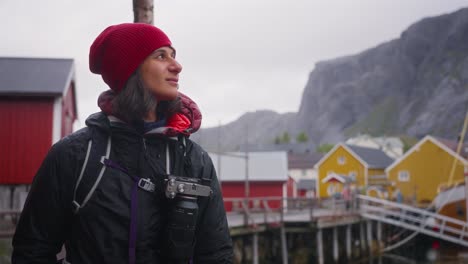 SLOW-MOTION-Truck-up-shot-of-a-young-female-photographer-tourist-and-her-golden-retriever-dog-photographing-the-beautiful-fisher-village-of-Å-and-its-red-rorbu-houses-in-the-Lofoten-Islands,-Norway