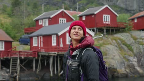 SLOW-MOTION-360-Orbit-around-a-young-female-photographer-tourist-admiring-the-beautiful-fisher-village-of-Å-and-its-red-rorbu-houses-in-the-Lofoten-Islands,-Norway