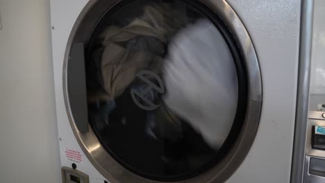 Side-loader-dryer-machine-spins-with-clothes-dropping-and-tumbling-in-laundromat