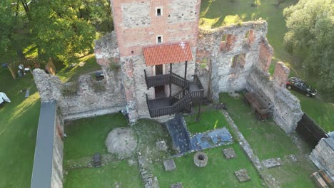 Medieval-Chudow-castle-with-a-walls,-tower,-and-courtyard-during-a-beautiful-summer-day-surrounded-by-lush-greenery,-grass,-and-trees-under-a-clear-blue-sky