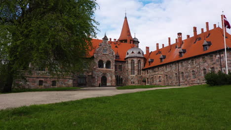 Cesvaines-castle-with-Latvia-flag-on-grassy-grounds-with-dirt-driveway-entrance
