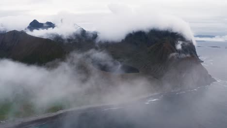 Vista-Aérea,-Atravesando-Las-Nubes-En-Un-Día-De-Mal-Humor,-Revelando-Un-Hermoso-Lago-Descansando-En-Las-Montañas-Sobre-El-Mar,-Cerca-De-Unstad,-Islas-Lofoten,-Noruega