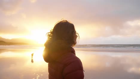 Zeitlupe,-Eine-Wunderschöne-Junge-Frau-Bewundert-Die-Aussicht-Und-Lächelt,-Mit-Wind-In-Ihren-Haaren,-Am-Strand-Von-Flakstad-Vor-Einem-Wunderschönen-Goldenen-Sonnenuntergang,-Lofoten-Inseln,-Norwegen