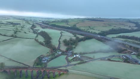 Derelict-stone-viaduct-bridge-and-M6-motorway-with-light-traffic-and-light-mist-and-fog-at-dawn-in-winter