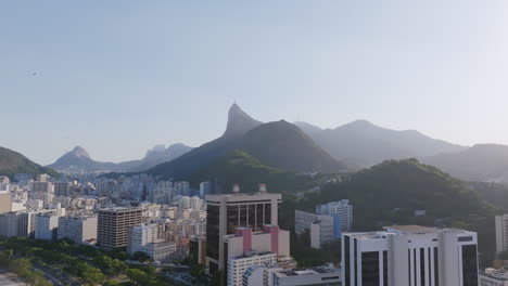 Pfeilaufnahmen-Fliegen-über-Die-Gebäude-Von-Botafogo-In-Rio-De-Janeiro,-Brasilien-Mit-Der-Christusstatue-Im-Hintergrund-Im-Dunst-Des-Morgenlichts