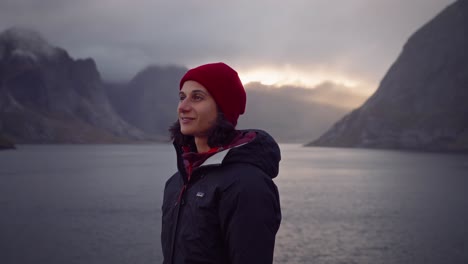 Orbit-shot-around-an-ecstatic-young-woman-smiling-while-admiring-the-sunset-in-Hamnøy,-Lofoten-Islands,-Norway