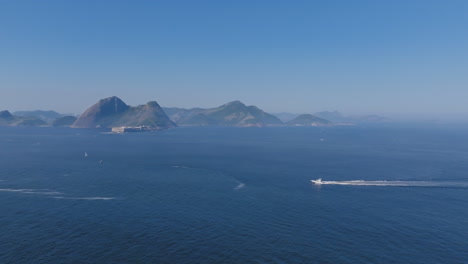 Aerial-footage-of-Farol-da-Fortaleza-de-Santa-Cruz-off-the-coast-of-Rio-de-Janeiro-with-a-sailboat-crossing-the-waters-in-front-of-it