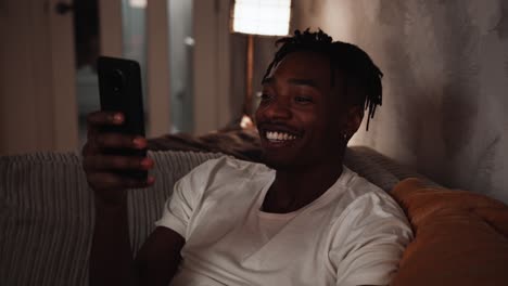 Young-black-male-smiles-and-shakes-his-head-while-looking-at-his-smart-phone