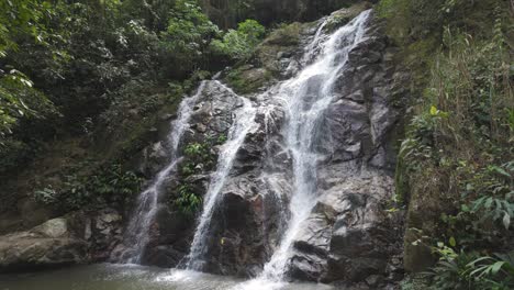 Peaceful-Marinka-waterfall-cascading-down-rocky-cliffs-into-a-tranquil-pool-in-a-lush-green-forest-setting,-Minca