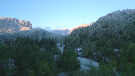 Una-Vista-Aérea-Del-Tranquilo-Paisaje-Invernal-De-Las-Montañas-Eslovenas-Con-árboles-Cubiertos-De-Nieve-Y-Un-Pequeño-Pueblo