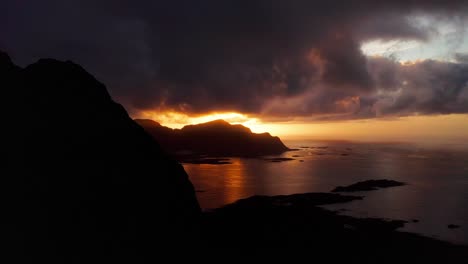 Aerial-view,-Revealing-the-beautiful-sunset-behind-the-mountains-of-Flakstad-surf-beach,-Lofoten-Islands,-Norway