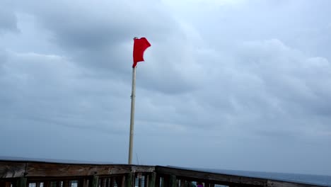 A-red-flag-flies-on-a-pier-in-the-wind-indicating-dangerous-surf-at-the-beach-in-Florida