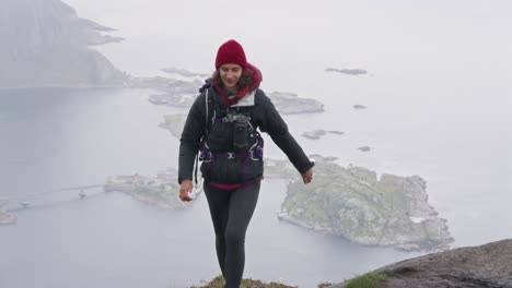 An-athletic-woman-arriving-at-the-top-of-Reinebringen-hike-with-a-view-of-Hamnøy-in-the-background,-Reine,-Lofoten-Islands,-Norway