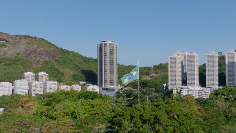 Breite-Zeitlupen-Luftaufnahmen,-Die-Sich-Um-Die-Im-Wind-Wehende-Brasilianische-Flagge-Im-Yitzhak-Rabin-Park-In-Rio-De-Janeiro-Drehen