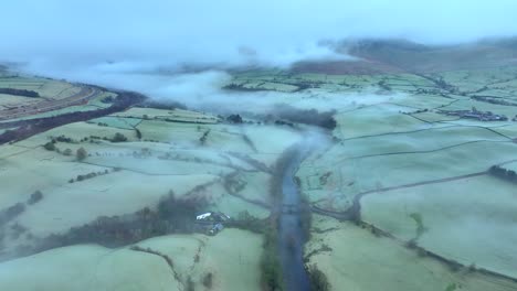 Mist-shrouded-meandering-river-amongst-patchwork-green-and-frost-covered-fields-at-dawn-in-winter