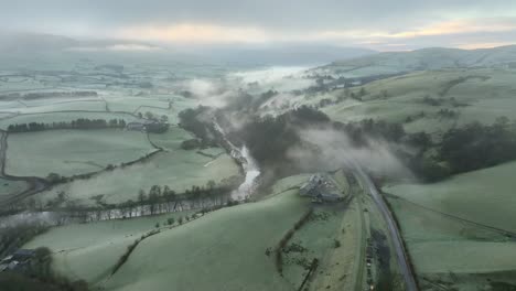 Fog-shrouded-landscape-with-meandering-river-amongst-patchwork-fields-at-dawn-in-winter