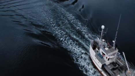 Aerial-view-tilting-down-on-a-fisher-boat-returning-to-port-under-the-Flakstadbruene-bridge,-near-Fredvang,-Lofoten-Islands,-Norway