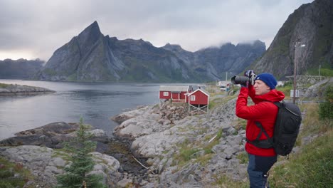 A-male-photographer-in-a-red-jacket-is-taking-a-picture-of-the-mountains-and-the-fjords-with-his-telephoto-lens-in-Hamnøy,-Lofoten-Islands,-Norway