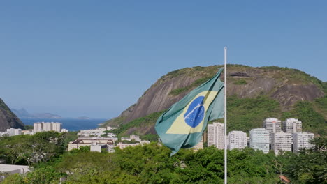 Luftaufnahmen-In-Super-Zeitlupe,-Die-Sich-Um-Die-Im-Wind-Wehende-Brasilianische-Flagge-Im-Yitzhak-Rabin-Park-In-Rio-De-Janeiro-Drehen
