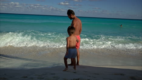Slow-motion-of-a-mexican-latin-brunette-man-with-beard-inviting-his-son-to-the-water-at-a-beach-in-Cancun-Mexico