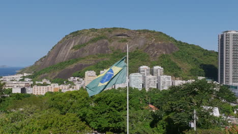 Zeitlupen-Luftaufnahmen,-Die-Sich-Um-Die-Im-Wind-Wehende-Brasilianische-Flagge-Im-Yitzhak-Rabin-Park-In-Rio-De-Janeiro-Drehen
