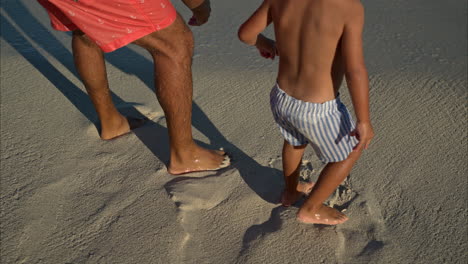 Close-up-of-the-legs-of-a-young-mexican-latin-boy-and-his-father-wearing-shorts-standing-on-the-sand-waiting-for-a-wave-in-Cancun