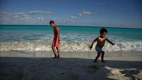 Young-mexican-latin-brunette-boy-running-away-from-the-waves-with-his-father-at-a-beach-in-Cancun-Mexico