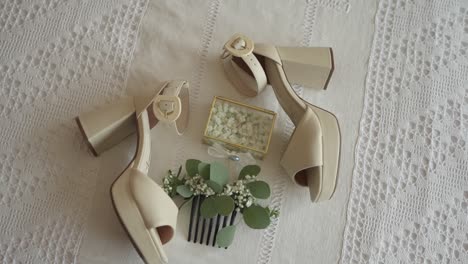 Pair-of-beige-high-heeled-shoes-with-floral-hair-accessory-and-jewelry-box-on-white-lace-fabric