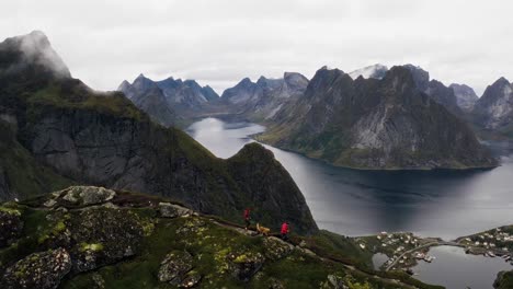 Aerial-view-of-an-athletic-couple-and-their-golden-retriever-dog-running-on-the-crest-of-Reinebringen-Hike-near-Reine,-Lofoten-Islands,-Norway